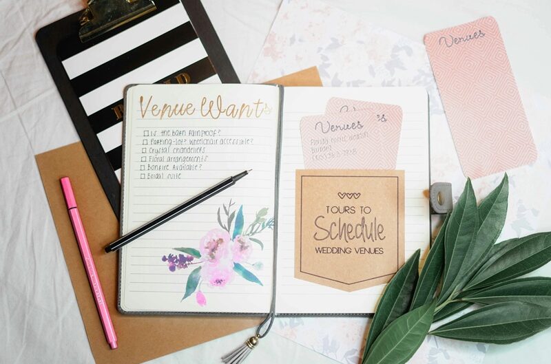 Open wedding planner notebook with a venue checklist, scheduling notes, and pens on a desk, helping couples organize their wedding venue tours.